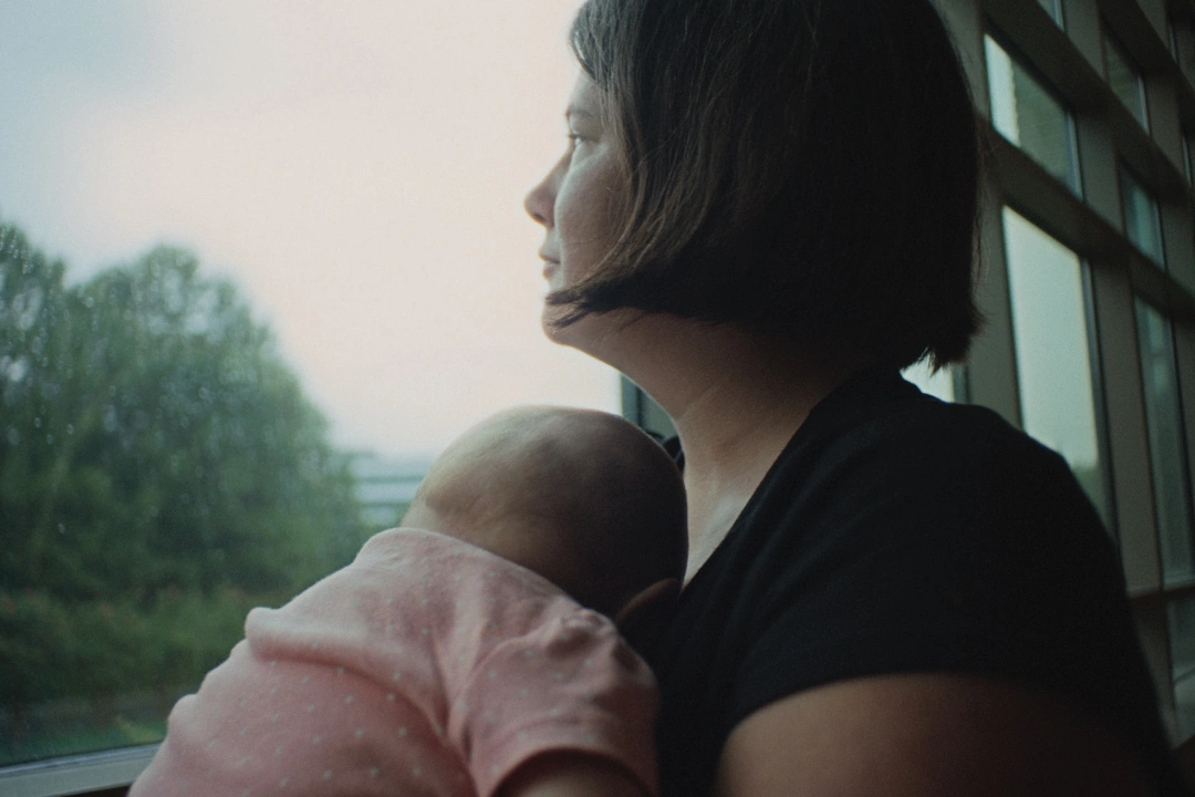 mother holding sleeping child closely, looking out window